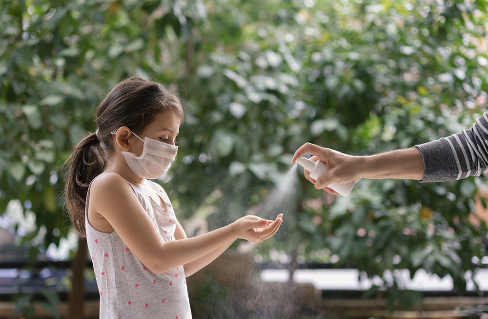 Father squirts antibacterial hand sanitizer in daughter's hands, Little girl wears a face mask during coronavirus and flu outbreak